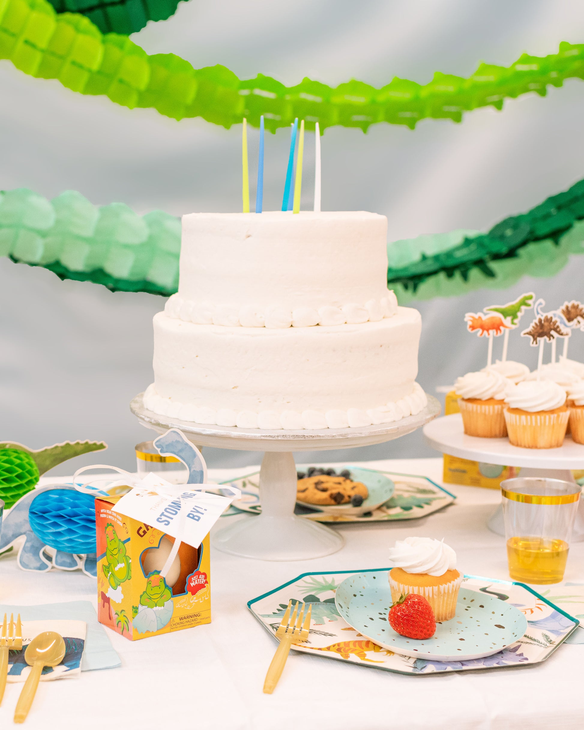 Kids dinosaur birthday party table with green and orange decor, dino figurines, and green garlands